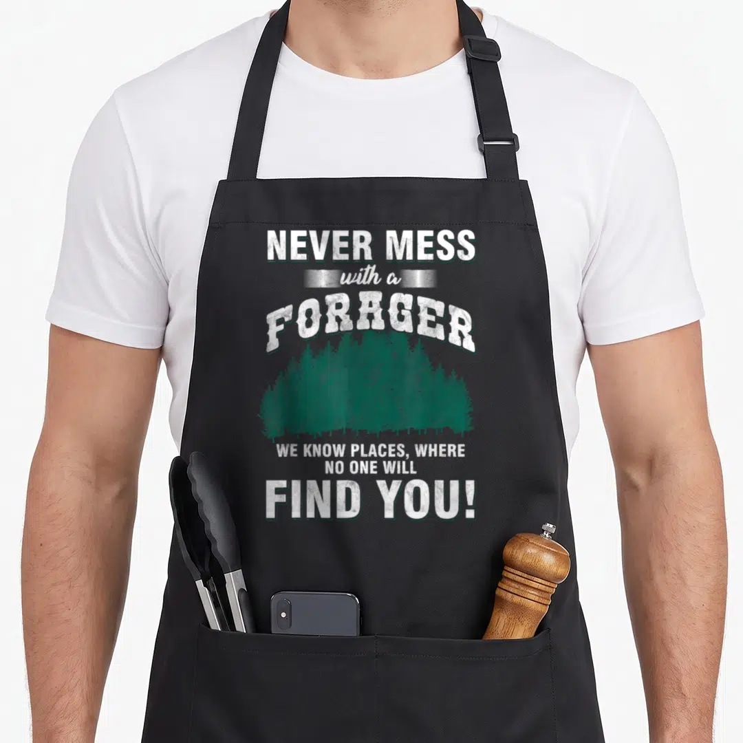 Mess foraging apron - White distressed text reading Never Mess With A Forager above a green forest silhouette — shown on a black cotton canvas apron against a white background