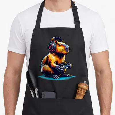 Rodent video game apron - Cartoon capybara wearing headphones and holding game controller in orange blue black art — shown on a black cotton canvas apron against a white background