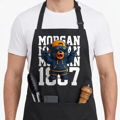 Gan apron or apron - Cartoon bear in blue hoodie and orange cap standing before stacked white MORGAN text and 1887 — shown on a black cotton canvas apron against a white background
