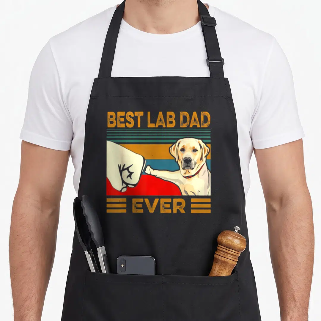 Lab owner father apron - Retro BEST LAB DAD EVER text above human hand fist bumping yellow labrador paw on striped — shown on a black cotton canvas apron against a white background