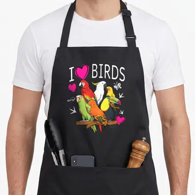Parrot cockatoo bird apron - Five colorful birds perched on brown branch with I BIRDS text and pink hearts — shown on a black cotton canvas apron against a white background