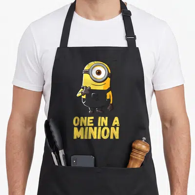 Funny despicable general apron - Yellow minion standing above two lines of yellow text reading one in a minion — shown on a black cotton canvas apron against a white background