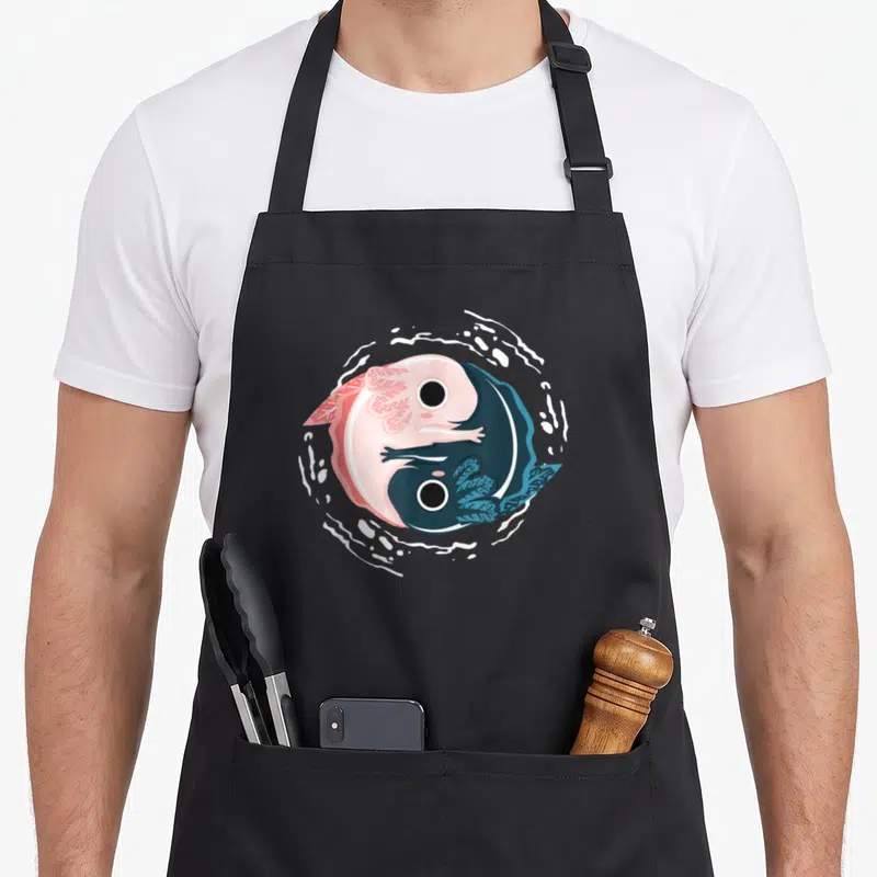 Yang yin yoga apron - Two curled axolotls in pink and blue forming a yin yang circle with white border — shown on a black cotton canvas apron against a white background