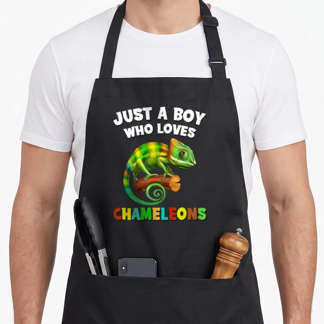 Cute chameleon apron - Cartoon chameleon in green and yellow perched on brown branch with multicolored text — shown on a black cotton canvas apron against a white background