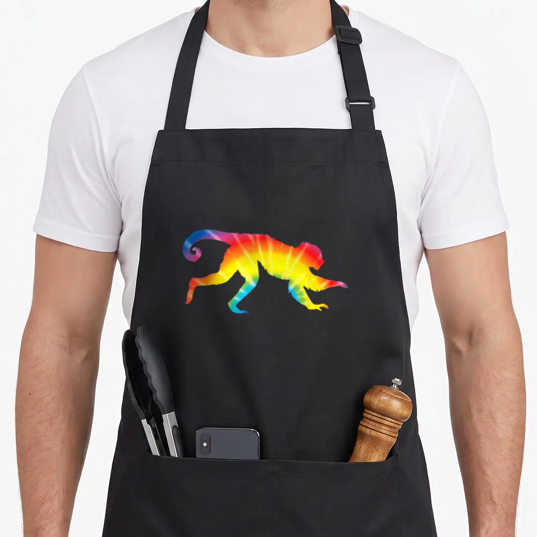 Lemur tie-dye apron - Rainbow tie-dye monkey silhouette in red, yellow, green, blue, and purple — shown on a black cotton canvas apron against a white background