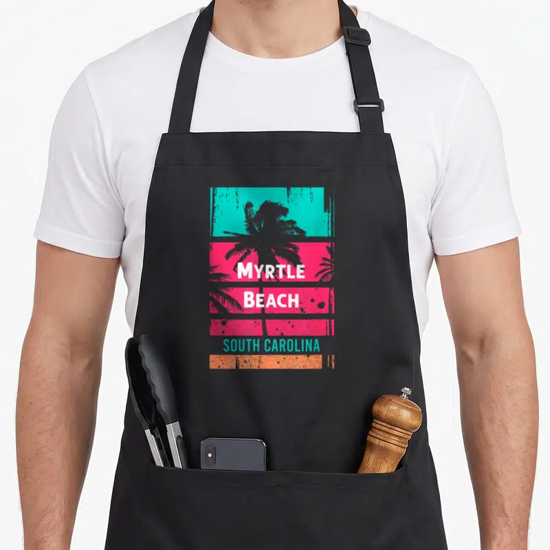 Souvenir south beach apron - Grey palm tree behind stacked cyan pink and orange distressed blocks with white MYRTLE — shown on a black cotton canvas apron against a white background