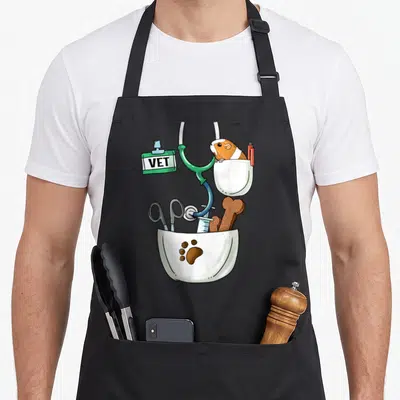 Veterinarian halloween apron - Guinea pig in white pocket with pen, medical tools below, green stethoscope, VET badge — shown on a black cotton canvas apron against a white background