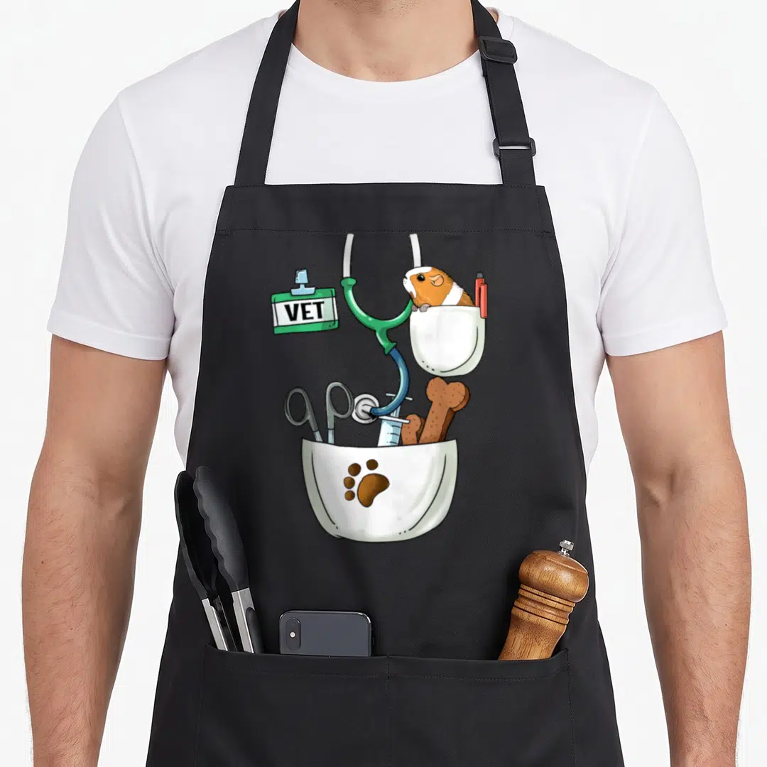 Veterinarian halloween apron - Guinea pig in white pocket with pen, medical tools below, green stethoscope, VET badge — shown on a black cotton canvas apron against a white background