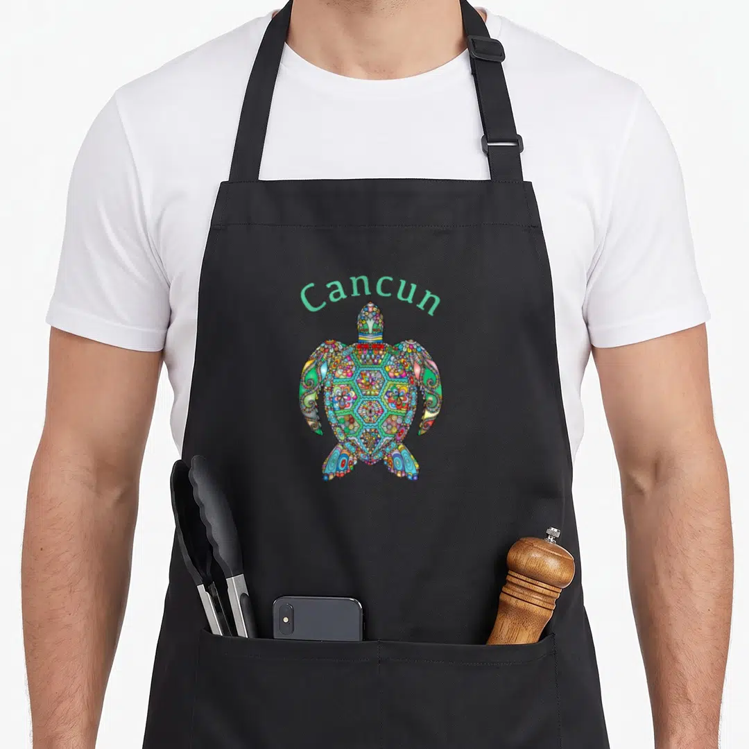 Tribal cancun apron - Cartoon sea turtle with tribal patterns and arched Cancun text in green and purple — shown on a black cotton canvas apron against a white background