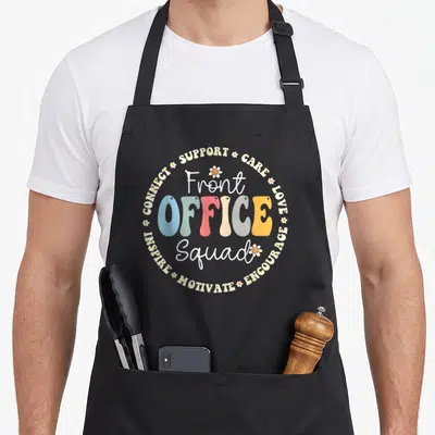 Appreciation office apron - Retro colorful Front Office Squad text surrounded by supportive words and daisies — shown on a black cotton canvas apron against a white background
