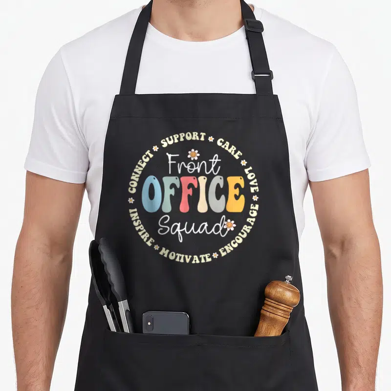Appreciation office apron - Retro colorful Front Office Squad text surrounded by supportive words and daisies — shown on a black cotton canvas apron against a white background