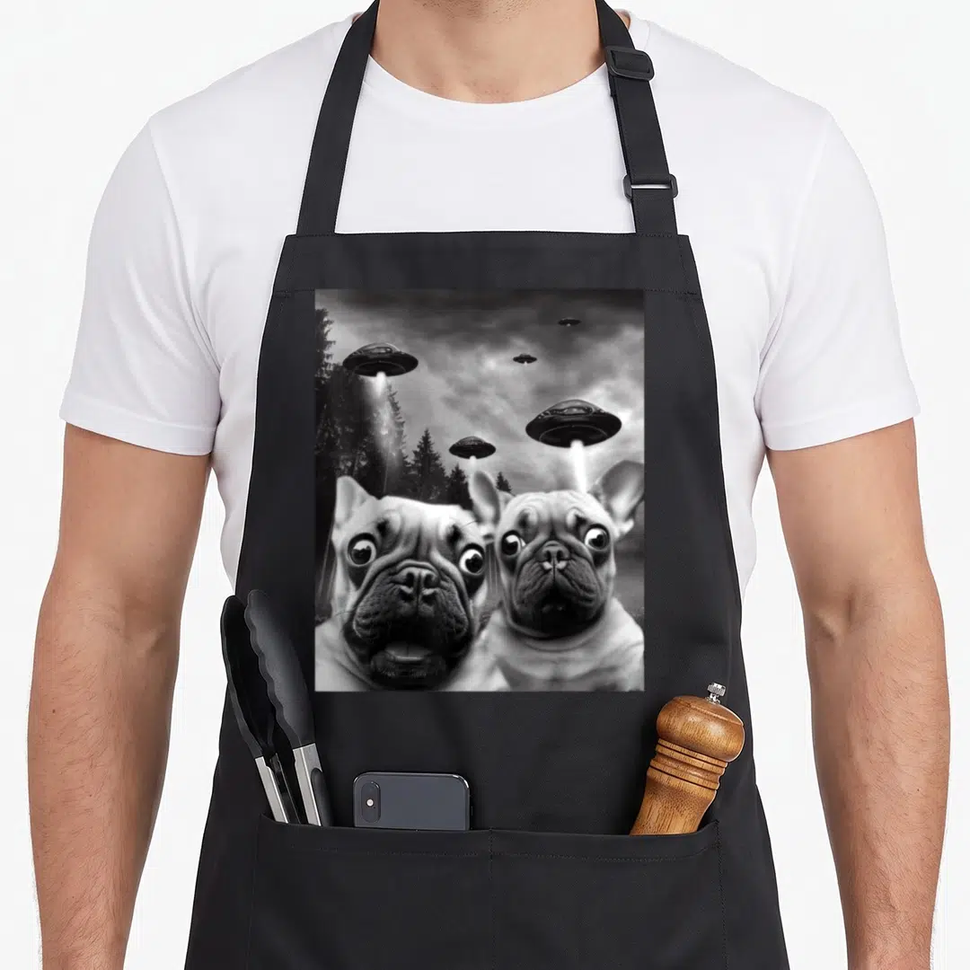 Ufo french bulldog apron - Two wide-eyed French Bulldogs with UFOs hovering over a forest in black and white photo art — shown on a black cotton canvas apron against a white background