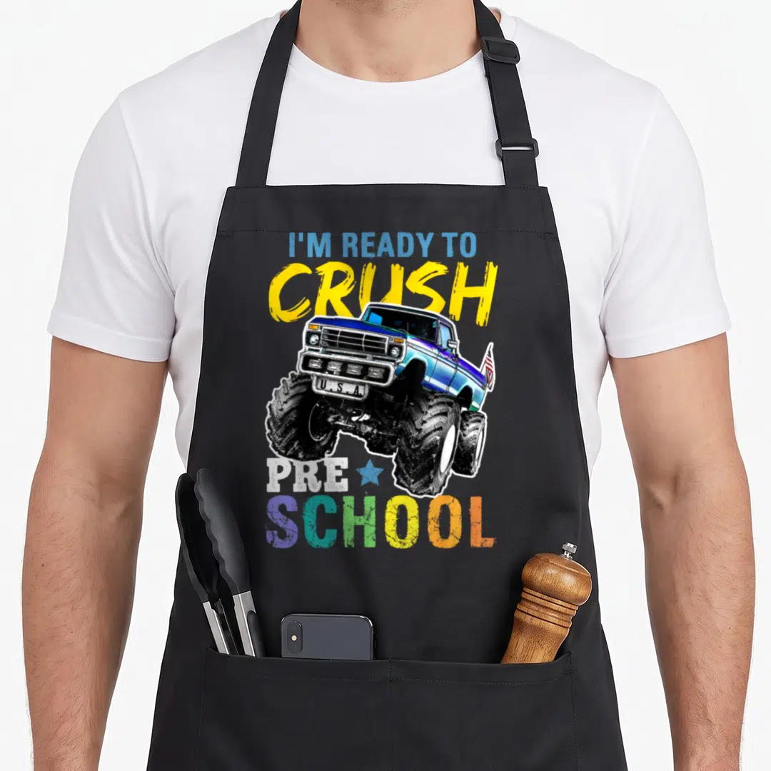 Crush preschool truck apron - Blue monster truck graphic with I'M READY TO CRUSH PRE SCHOOL text and USA license plate — shown on a black cotton canvas apron against a white background