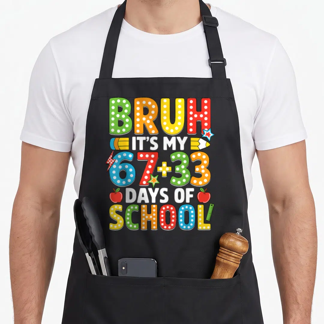 Bruh school apron - Colorful 67+33 days of school text with pencils apples and ruler — shown on a black cotton canvas apron against a white background