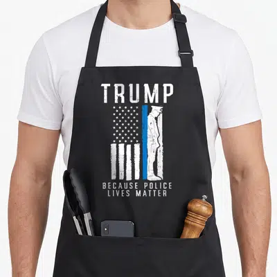 Live police apron - TRUMP text above distressed flag with officer silhouette and Because Police Lives Matter caption — shown on a black cotton canvas apron against a white background