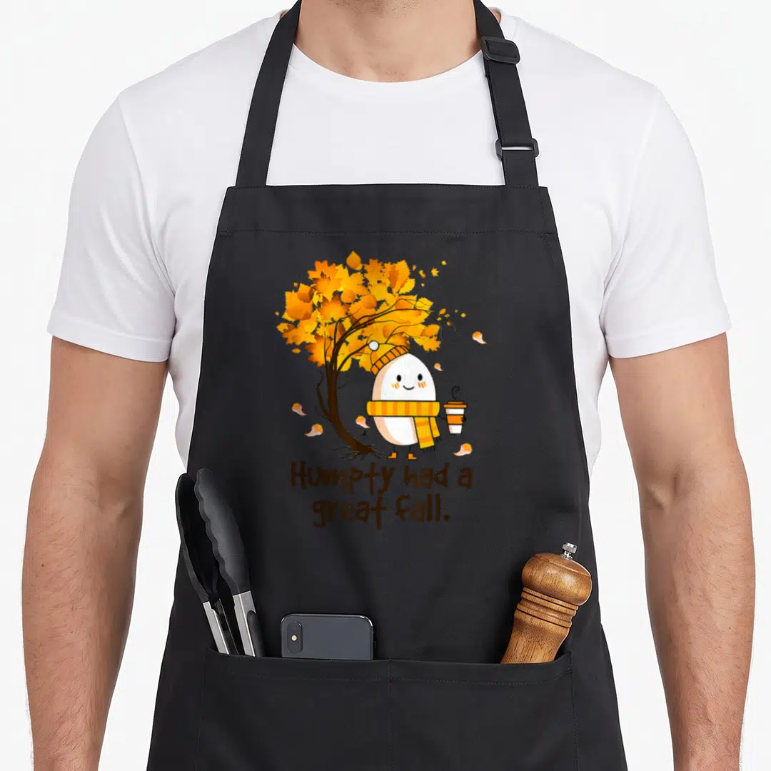 Humpty cute fall aprons - Egg character in scarf holding coffee under orange tree with Humpty had a great fall text — shown on a black cotton canvas apron against a white background