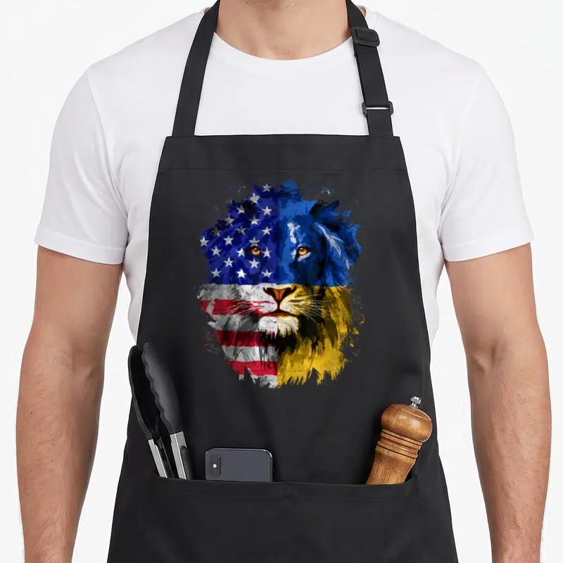Lion american flag apron - Watercolor lion head split vertically with USA stars stripes and Ukraine blue yellow colors — shown on a black cotton canvas apron against a white background