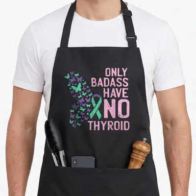Thyroid badass apron - Teal ribbon, pink text, purple and teal butterflies on black bib — shown on a black cotton canvas apron against a white background