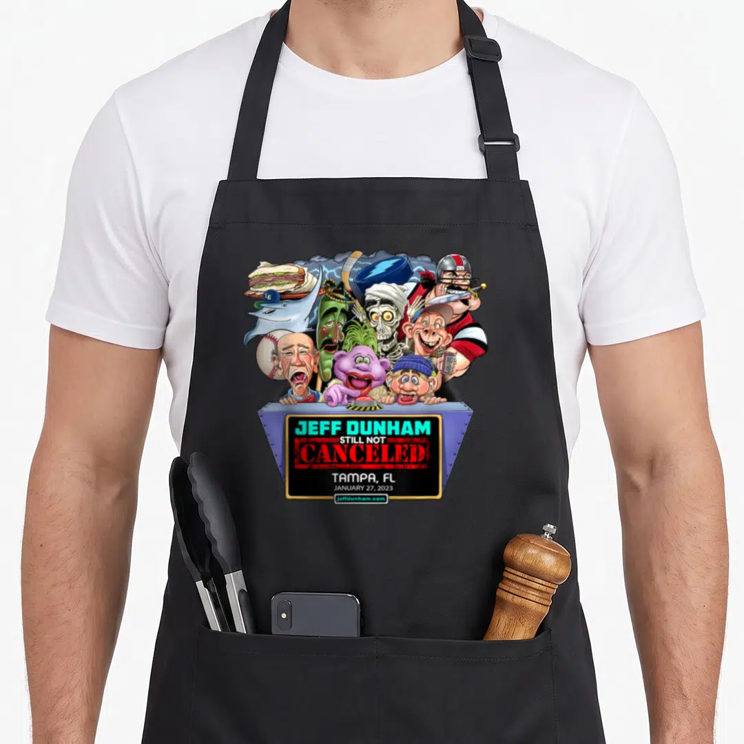 Jeff cartoon apron - Caricature cluster above blue sign reading Jeff Dunham Still Not Canceled Tampa FL Jan 27 2023 — shown on a black cotton canvas apron against a white background