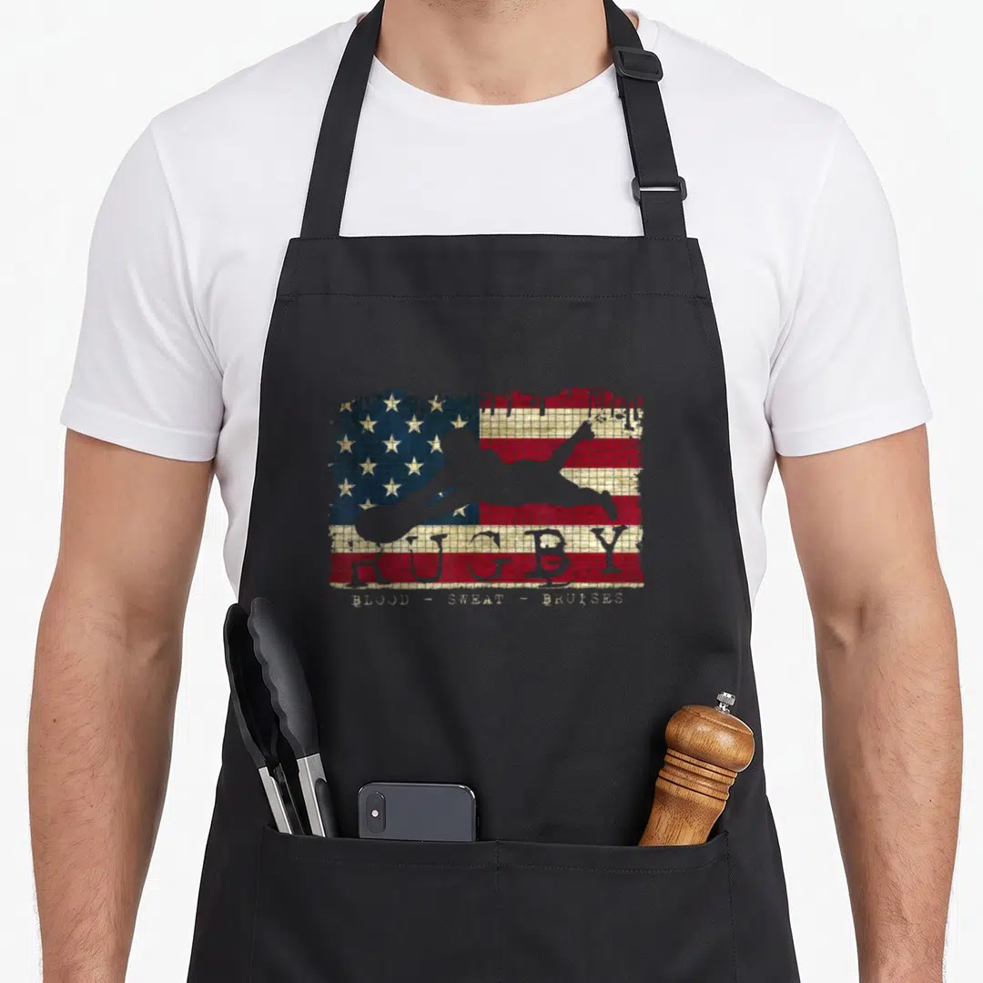 Flag blood apron - Rugby player silhouette over distressed USA flag with Blood Sweat Bruises text — shown on a black cotton canvas apron against a white background