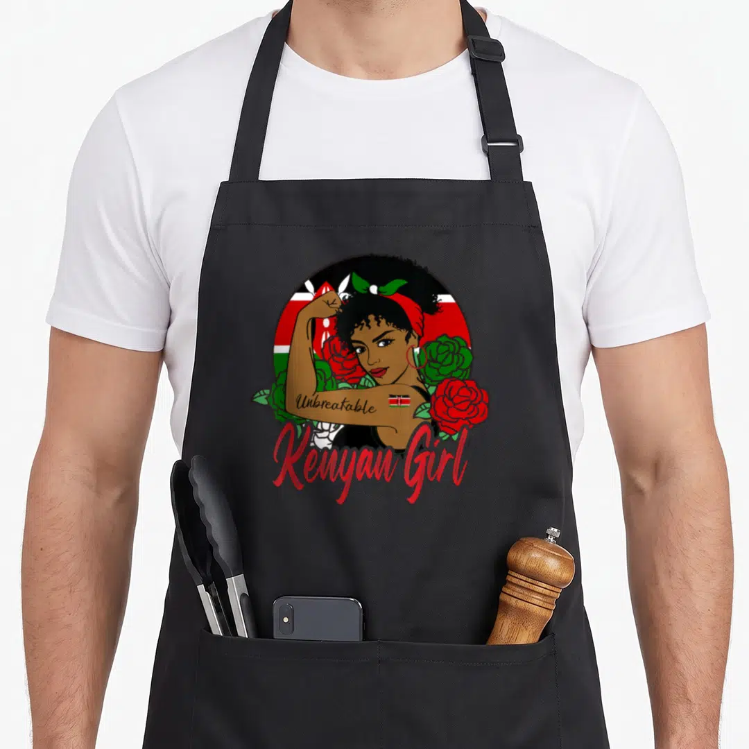 Kenya flag kenyan apron - Cartoon woman flexing arm with Unbreakable text and Kenyan Girl script surrounded by red — shown on a black cotton canvas apron against a white background