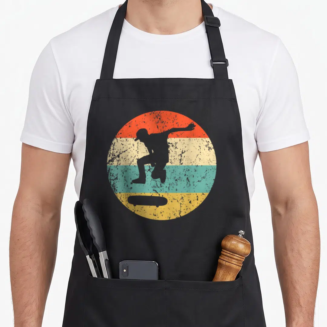 Funny skateboard apron - Grey skater silhouette inside orange cream teal and yellow striped circle — shown on a black cotton canvas apron against a white background