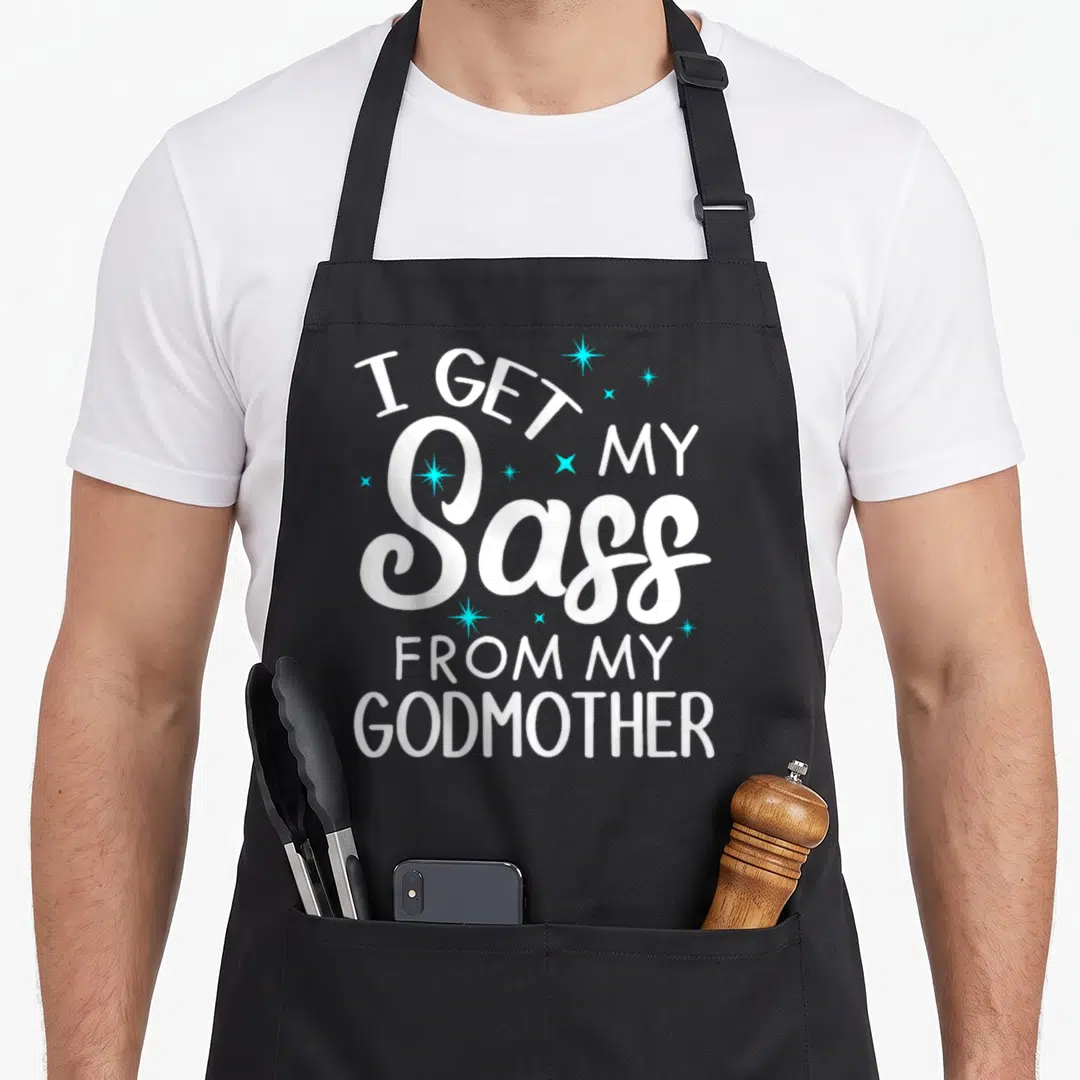 Sass goddaughter apron - I GET MY SASS FROM MY GODMOTHER text with light blue sparkles — shown on a black cotton canvas apron against a white background