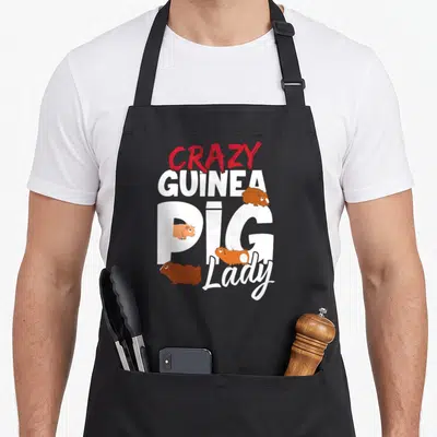 Vintage pig crazy guinea lady apron - Stacked CRAZY GUINEA PIG Lady text with four cartoon guinea pigs in red white — shown on a black cotton canvas apron against a white background