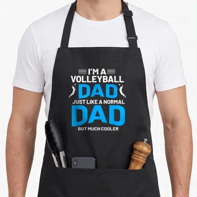 Cute volleyball dad apron - Stacked text I'M A VOLLEYBALL DAD with two white jumping player silhouettes flanking — shown on a black cotton canvas apron against a white background