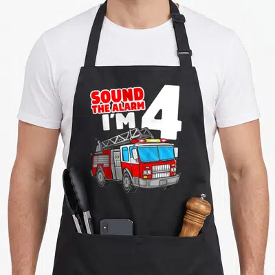 Four truck apron - SOUND THE ALARM I'M 4 text with red and white cartoon fire truck ladder illustration — shown on a black cotton canvas apron against a white background