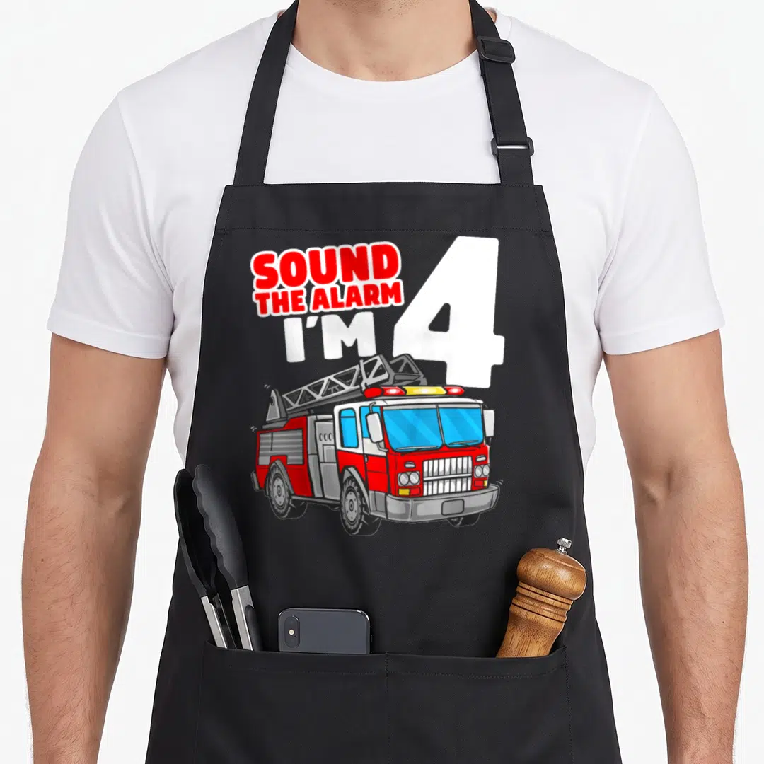 Four truck apron - SOUND THE ALARM I'M 4 text with red and white cartoon fire truck ladder illustration — shown on a black cotton canvas apron against a white background