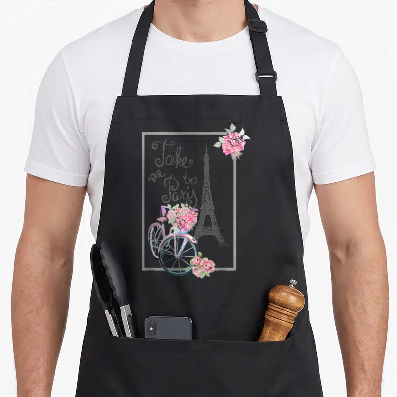 Paris french apron - Watercolor Eiffel Tower, bicycle with pink roses, and script text Take me to Paris inside a white — shown on a black cotton canvas apron against a white background
