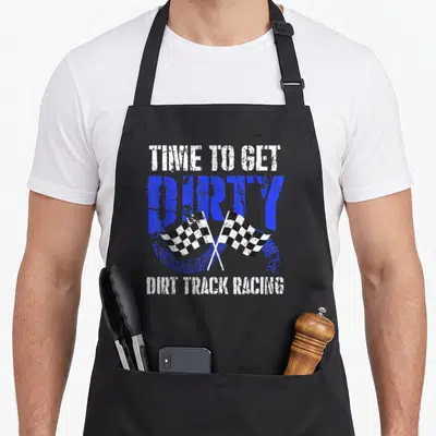 Dirty track apron - Stacked distressed text with two crossed checkered flags over a blue tire track circle — shown on a black cotton canvas apron against a white background