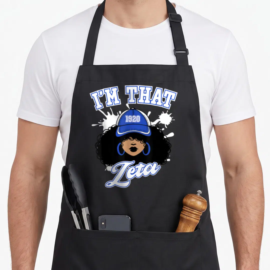 Zeta homecoming life apron - I'M THAT 1920 Zeta cartoon woman with blue cap and white splatter — shown on a black cotton canvas apron against a white background