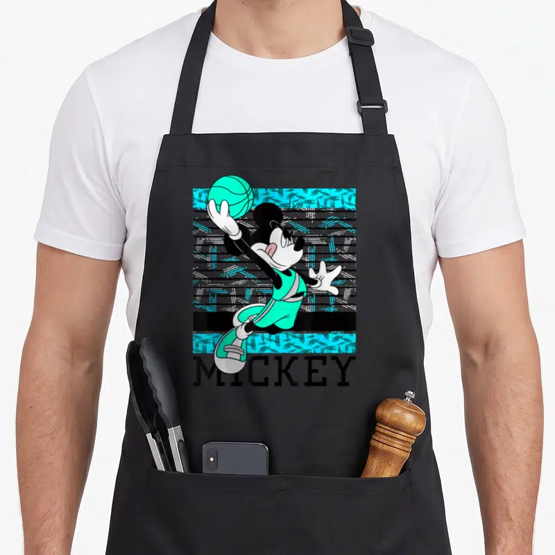 Funny basketball boys apron - Mickey Mouse in teal jersey reaching for basketball above MICKEY text on striped — shown on a black cotton canvas apron against a white background