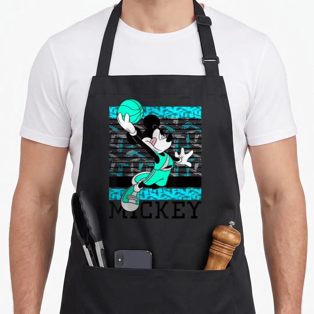 Funny basketball boys apron - Mickey Mouse in teal jersey reaching for basketball above MICKEY text on striped — shown on a black cotton canvas apron against a white background