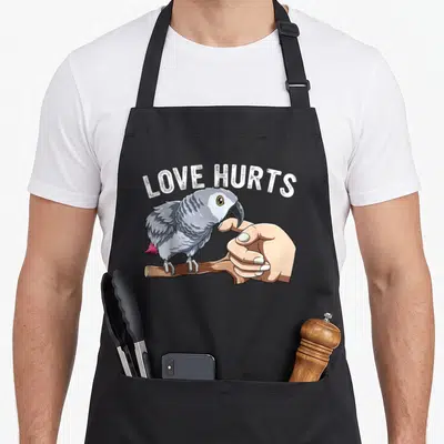 Hurt african aprons - Grey parrot perched on branch biting finger under arched LOVE HURTS text — shown on a black cotton canvas apron against a white background