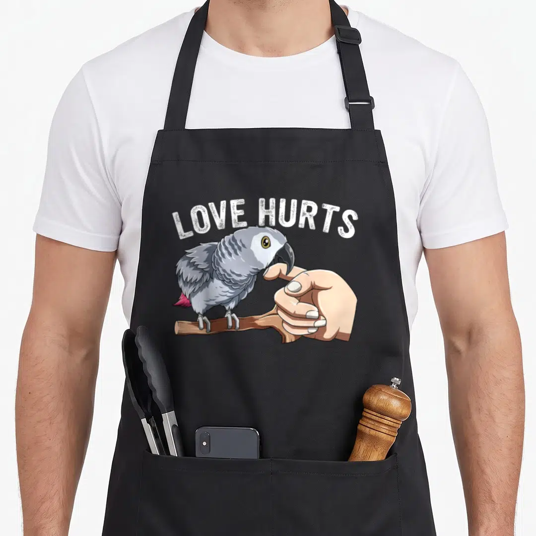 Hurt african aprons - Grey parrot perched on branch biting finger under arched LOVE HURTS text — shown on a black cotton canvas apron against a white background