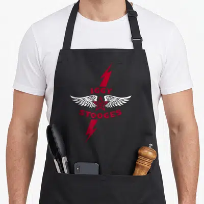Iggy pop apron - Red star with white wings and two lightning bolts surrounding red text IGGY AND THE STOOGES — shown on a black cotton canvas apron against a white background