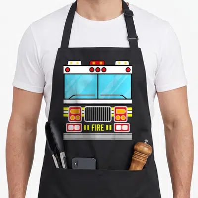 Fire easy apron - Cartoon fire truck front with white, red, yellow, blue lights and FIRE text on bumper — shown on a black cotton canvas apron against a white background