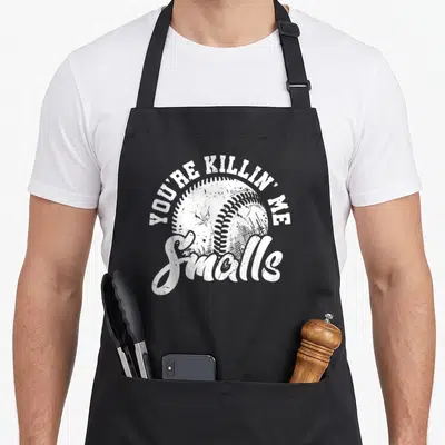 Killin softball apron - White distressed baseball with arched text YOU'RE KILLIN' ME and script Smalls below — shown on a black cotton canvas apron against a white background