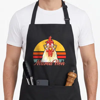 Mama hen aprons - Retro chicken wearing pink glasses and red polka dot bandana in front of striped sun — shown on a black cotton canvas apron against a white background
