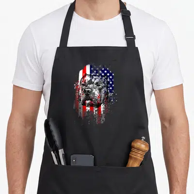 Pitbull patriotic apron - Distressed black line art pitbull head over red white blue paint splatter flag — shown on a black cotton canvas apron against a white background