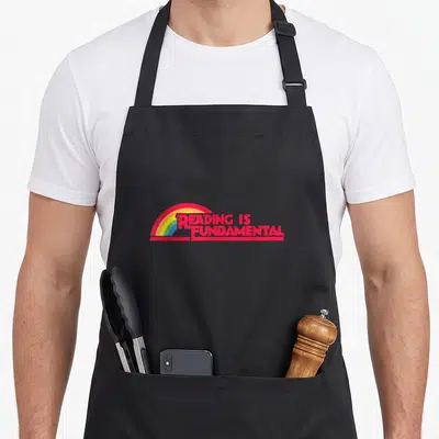 Reading gay apron - Red reading is fundamental text over rainbow arc on black background — shown on a black cotton canvas apron against a white background