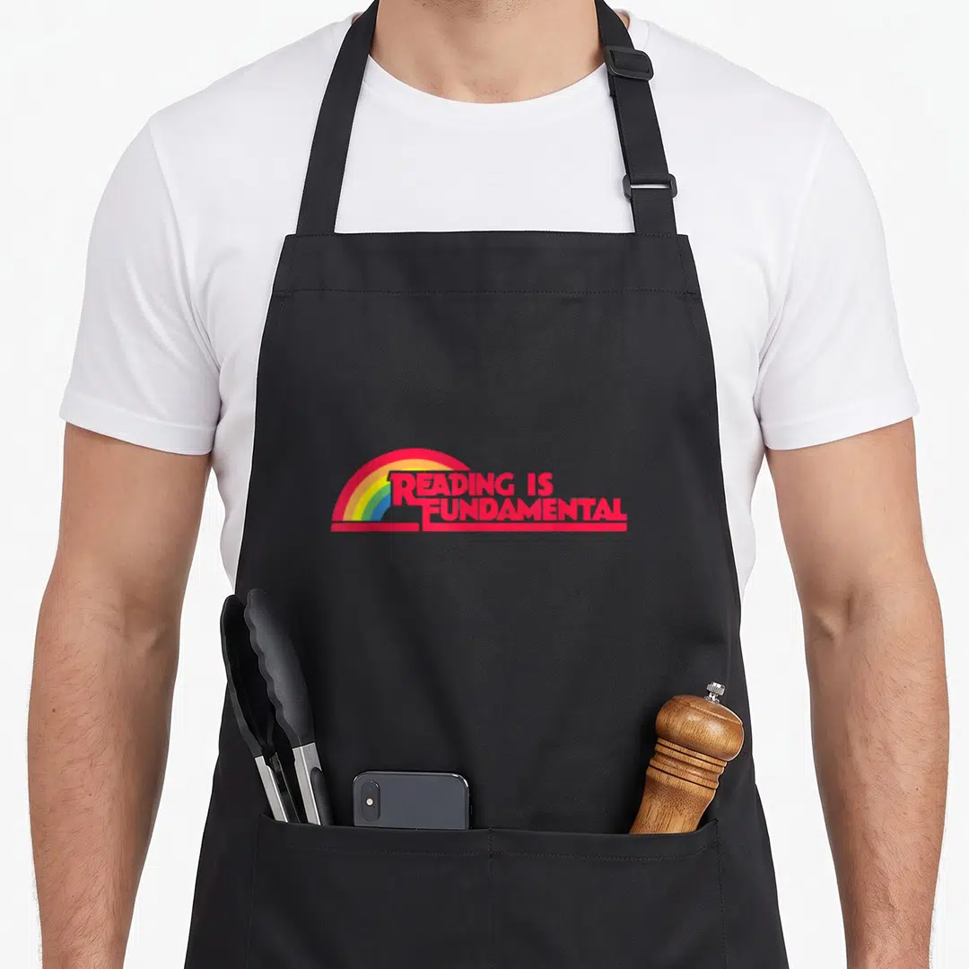 Reading gay apron - Red reading is fundamental text over rainbow arc on black background — shown on a black cotton canvas apron against a white background