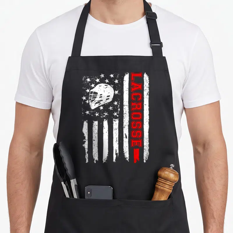 Lacrosse american flag apron - Distressed white and red flag with white helmet and vertical red LACROSSE text — shown on a black cotton canvas apron against a white background