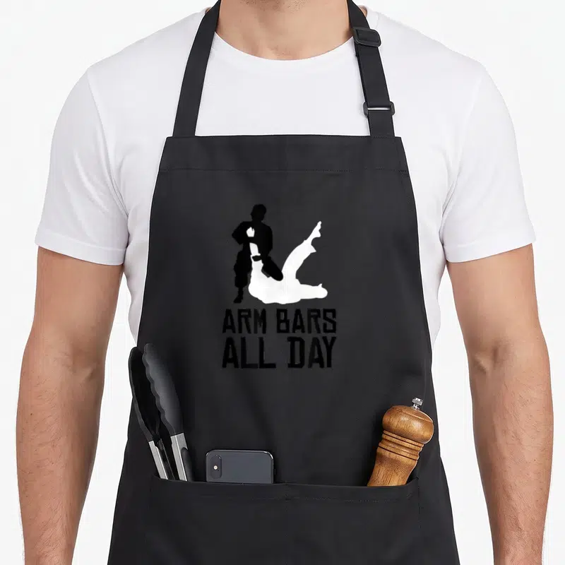 Bar arm day apron - Black and white grappling silhouette above stacked text ARM BARS ALL DAY — shown on a black cotton canvas apron against a white background