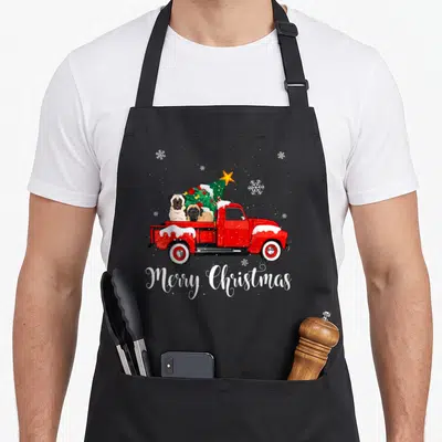 Mastiff red christmas apron - Red truck carrying two dogs and a Christmas tree with white text — shown on a black cotton canvas apron against a white background