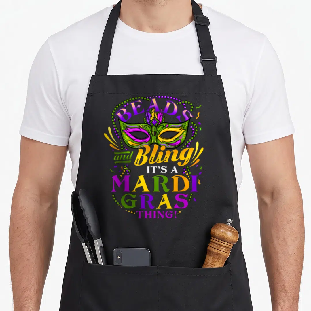 Funny mardi gras aprons - Masquerade mask surrounded by beads and confetti with printed text BEADS and Bling IT'S — shown on a black cotton canvas apron against a white background