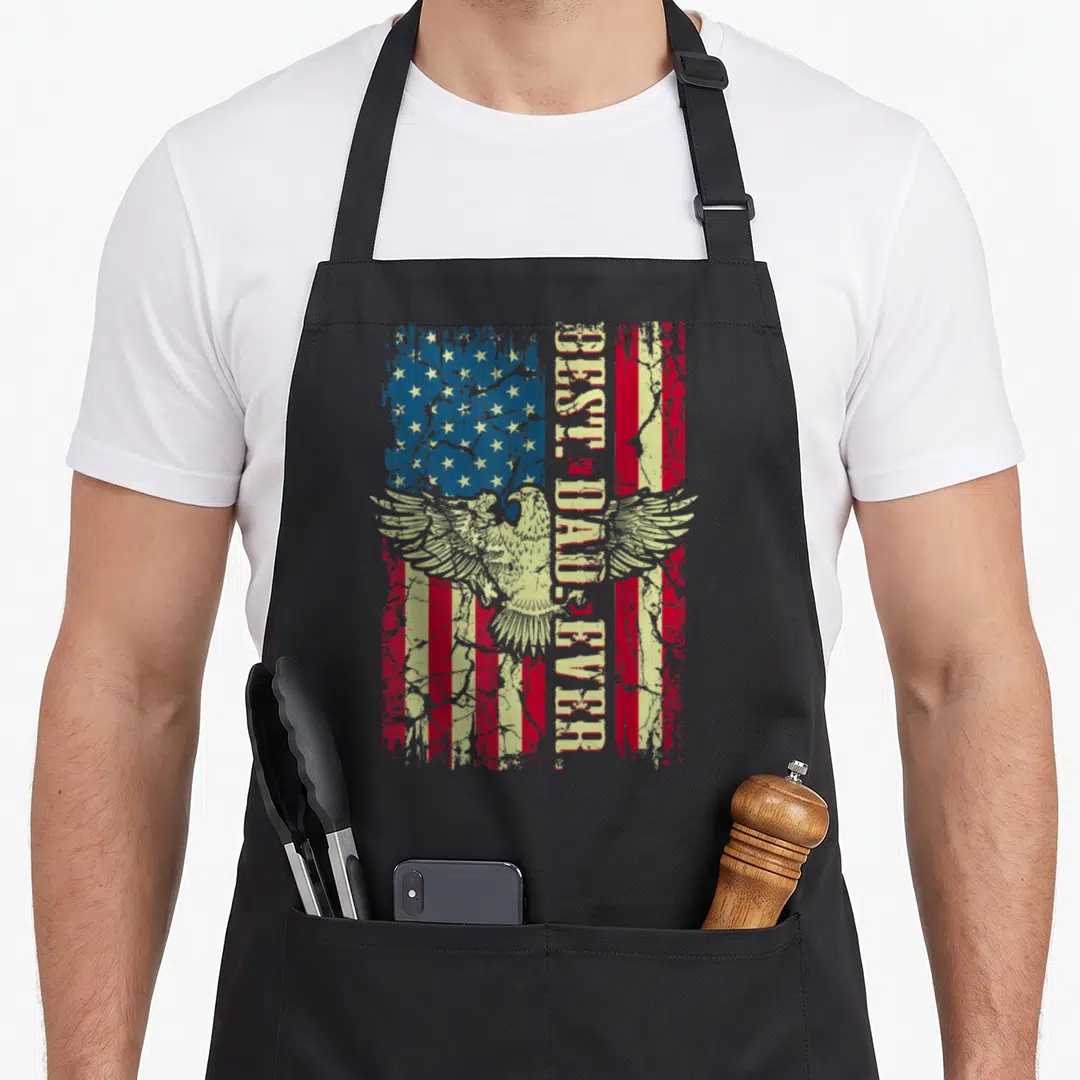 Father eagles apron - Distressed eagle superimposed over red white blue flag with vertical best dad ever text — shown on a black cotton canvas apron against a white background